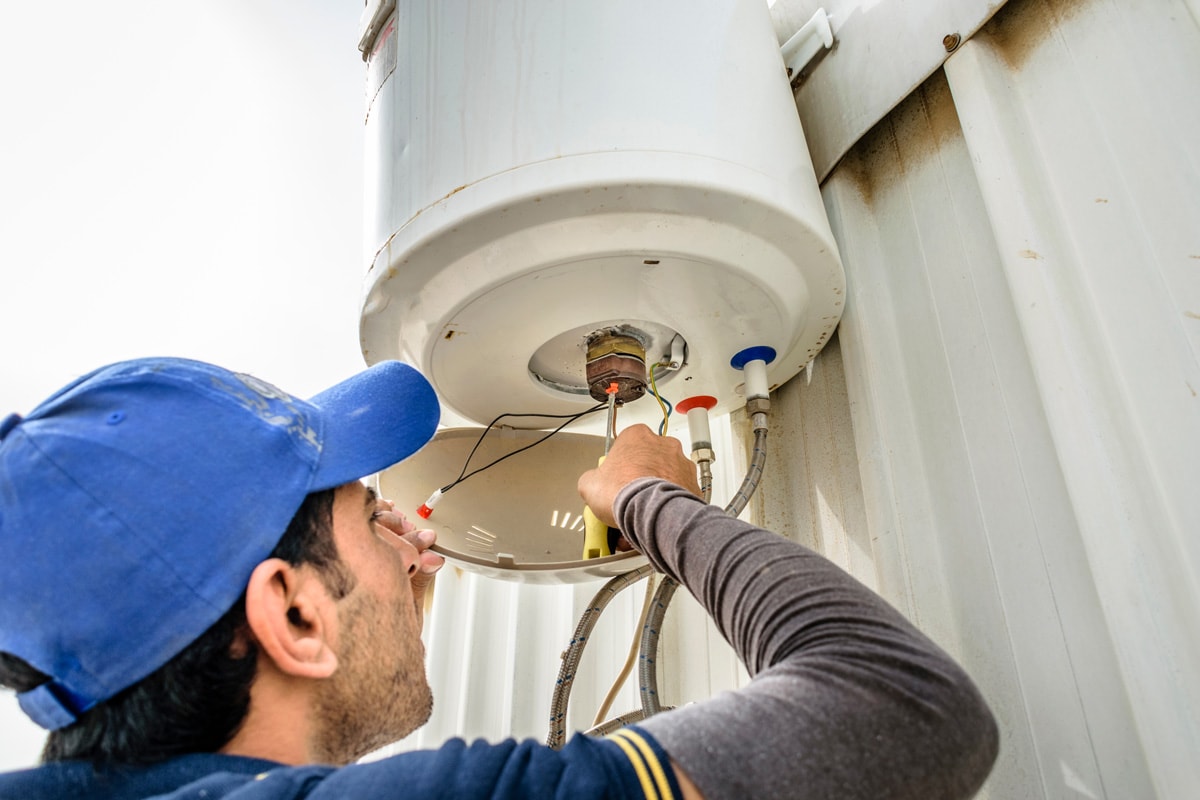a professional electrician man is fixing a water heater at the roof top and wearing blue uniform and cap