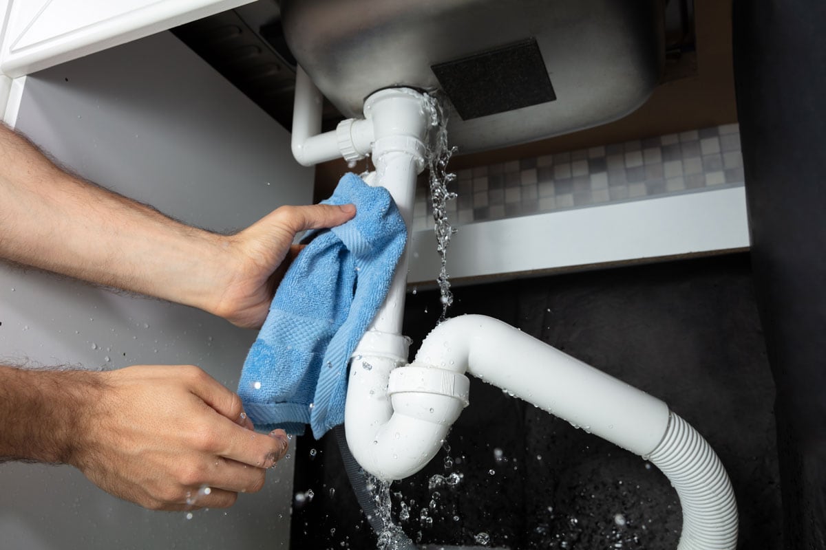 A Man's Hand Holding Blue Napkin Under Leakage Pipe