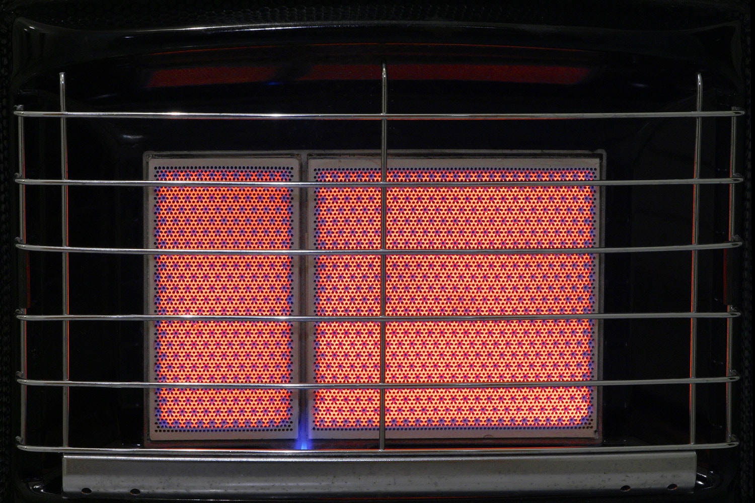 A close up of the heating ceramic of a switched on gas heater, with visible grill

