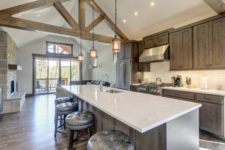 Amazing modern and rustic luxury kitchen with vaulted ceiling and wooden beams, long island with white quarts countertop and dark wood cabinets., How Much Does It Cost To Vault Or Raise A Ceiling In Specific Areas Of Your House? [Inc. Living Area, Bathroom, Kitchen, Bedroom, Garage, & Basement]