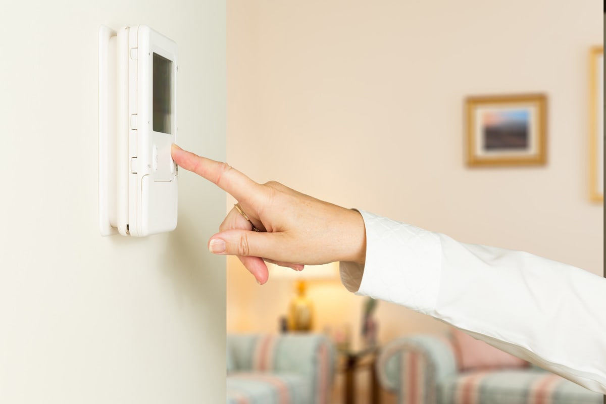 Caucasian female hand pressing button on a modern electronic thermostat timer on wall