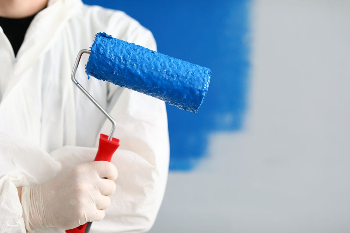 Close-up of person painter holding roller covered in blue paint.