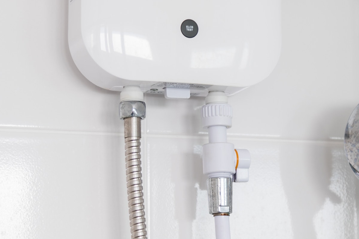 Instant tankless electric water heater installed on white tile wall 