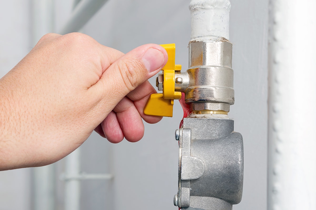 Person's hand opens or closes yellow gas valve on gas pipe at home