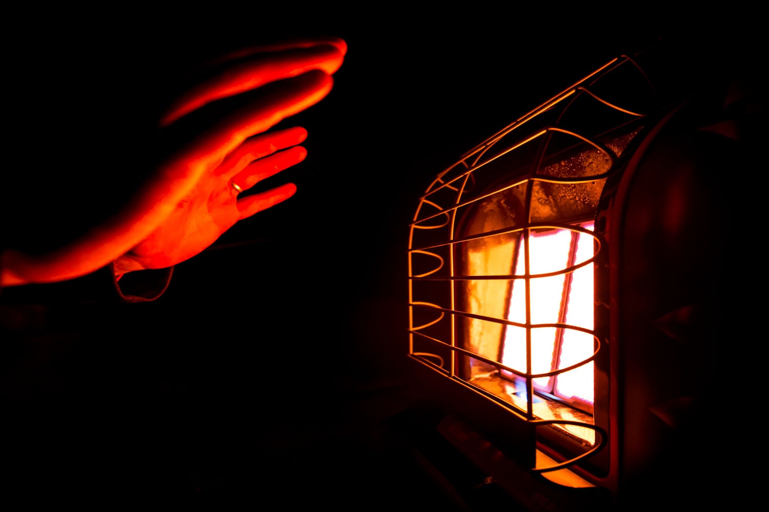 The warm glow reflecting off a heating element while warming up hands on a small space heating gas heater in a dark area. 