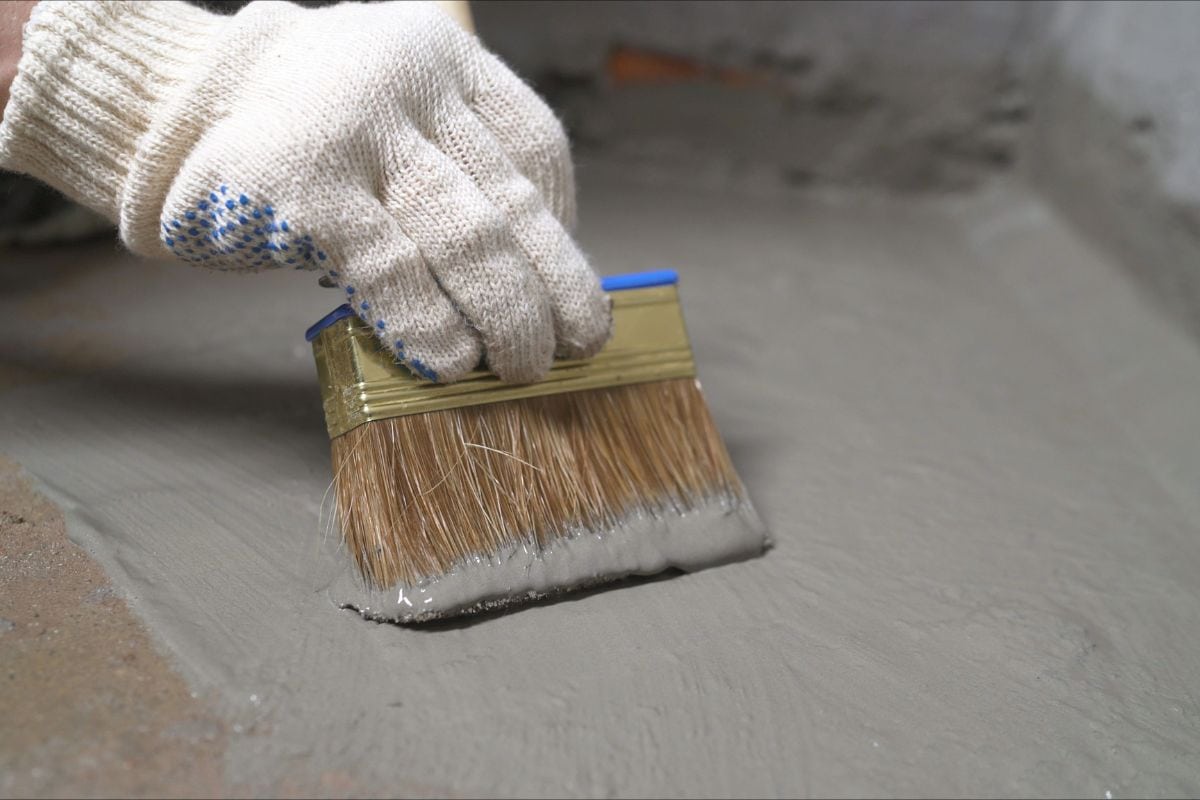 Workers cover the concrete screed with mortar and make waterproofing. The process of waterproofing the floor with a solution.
