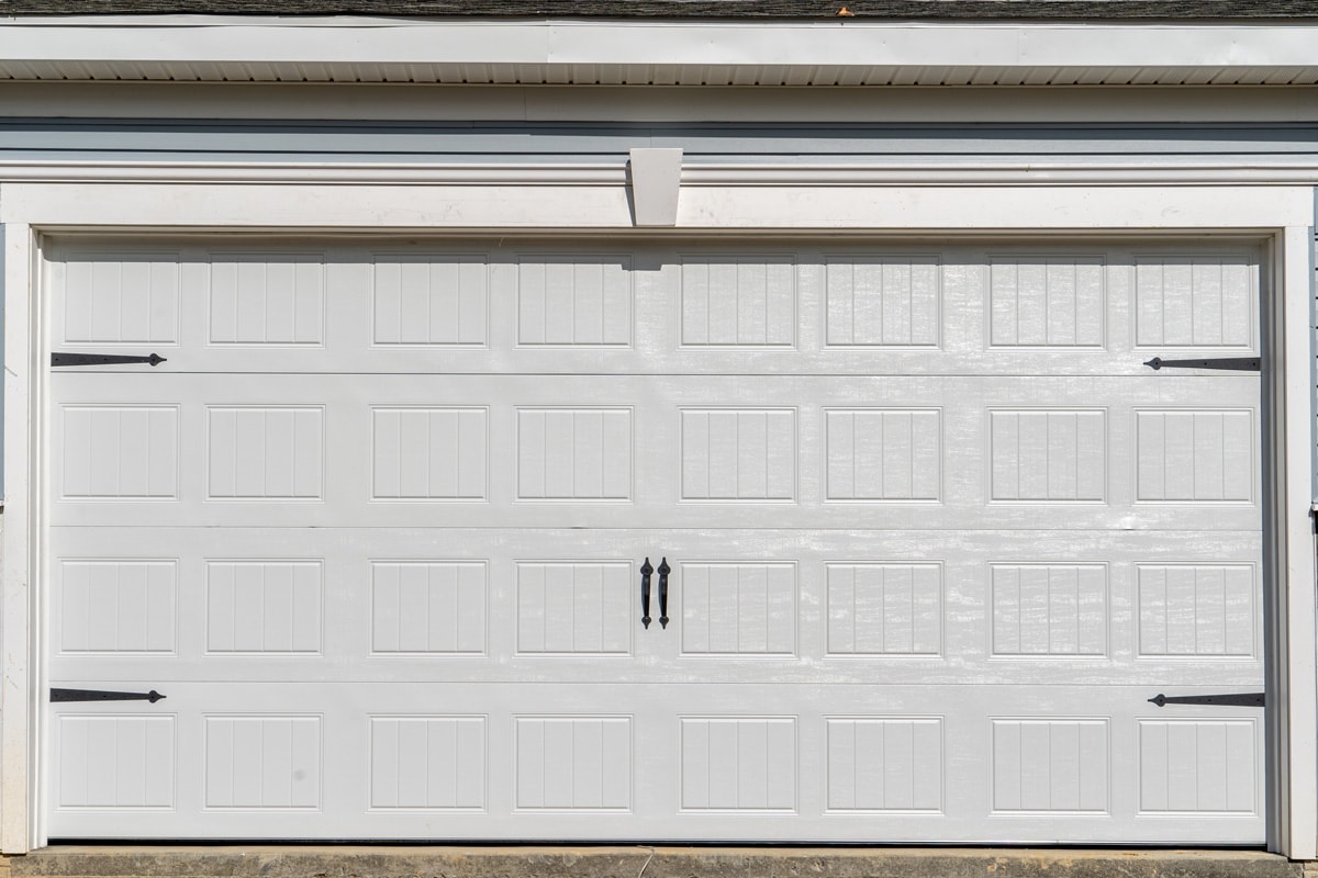 Double car classic insulated steel raised panel garage door framed with a white trim to add accent, on a new American home