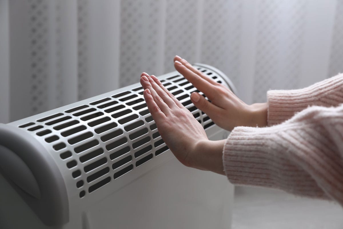 Woman warming hands near electric heater at home, closeup