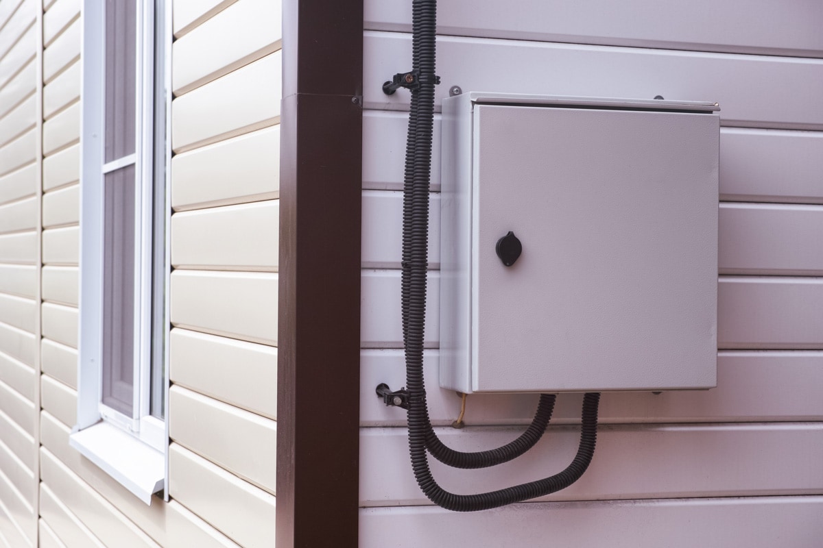 A gray electrical panel mounted outside the house exterior.