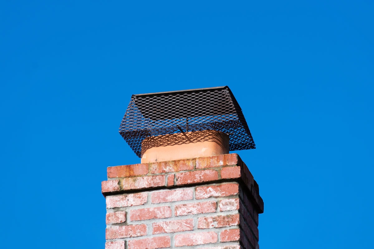 Chimney cap installed to prevent rodent entry to home, attic, building. Brick chimney. Blue sky.
