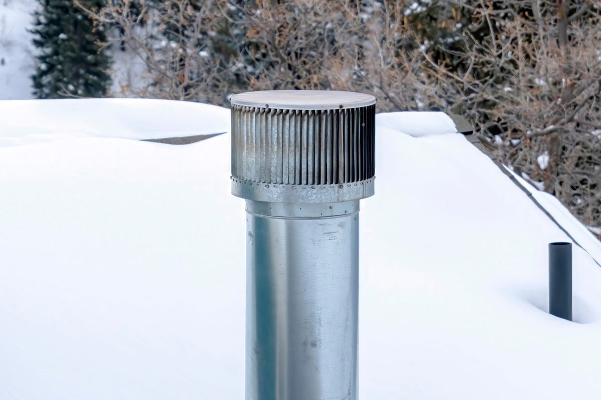 Shiny metal chimney vent pipe on the roof of home covered with snow in winter