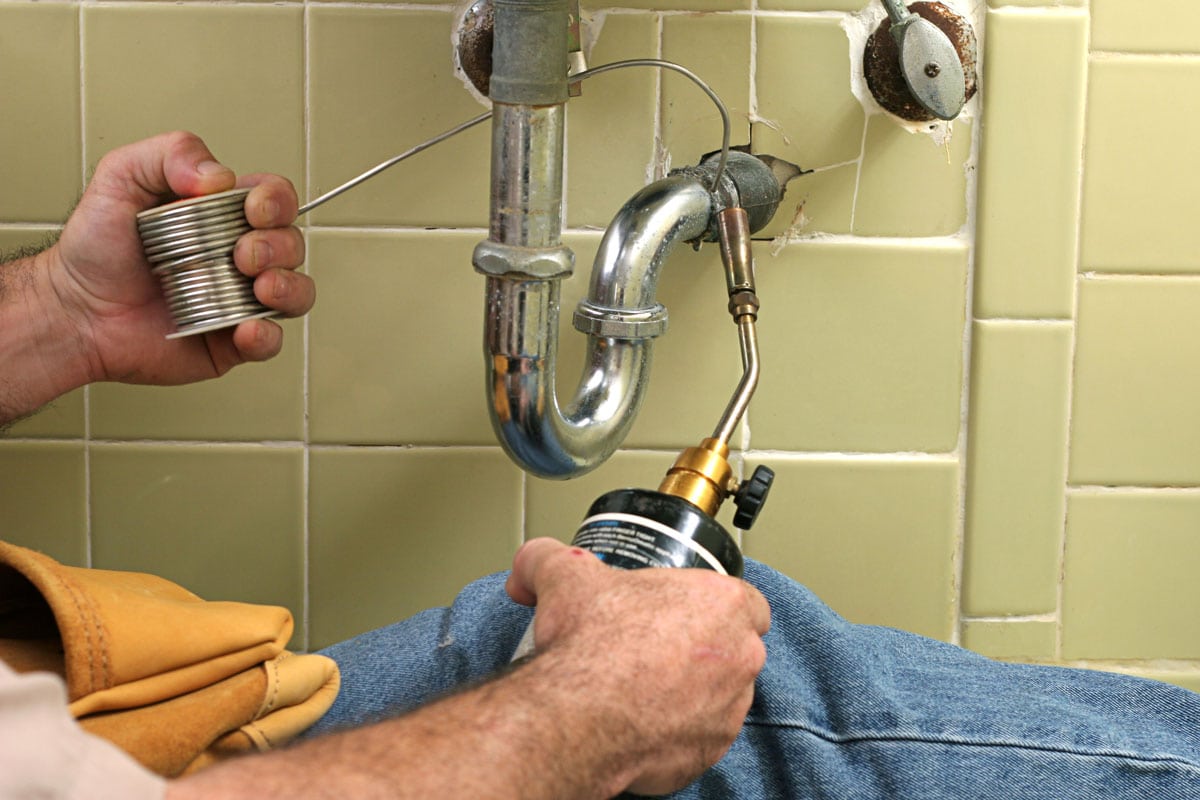 Mechanic using a blowtorch to solder a lavatory pipe