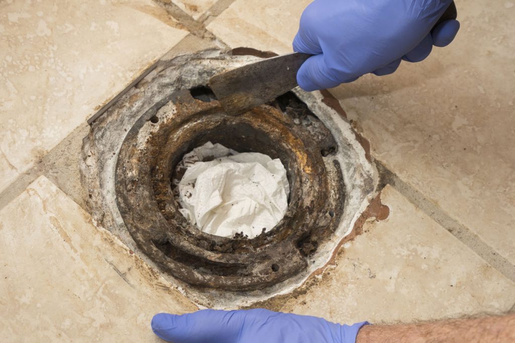 Closeup of man's hand scraping cast iron toilet flange with caulked lead joint
