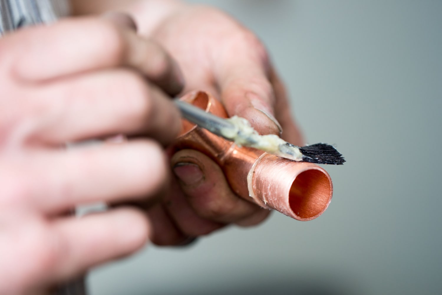 hand holding a brush applying flux on a copper pipe