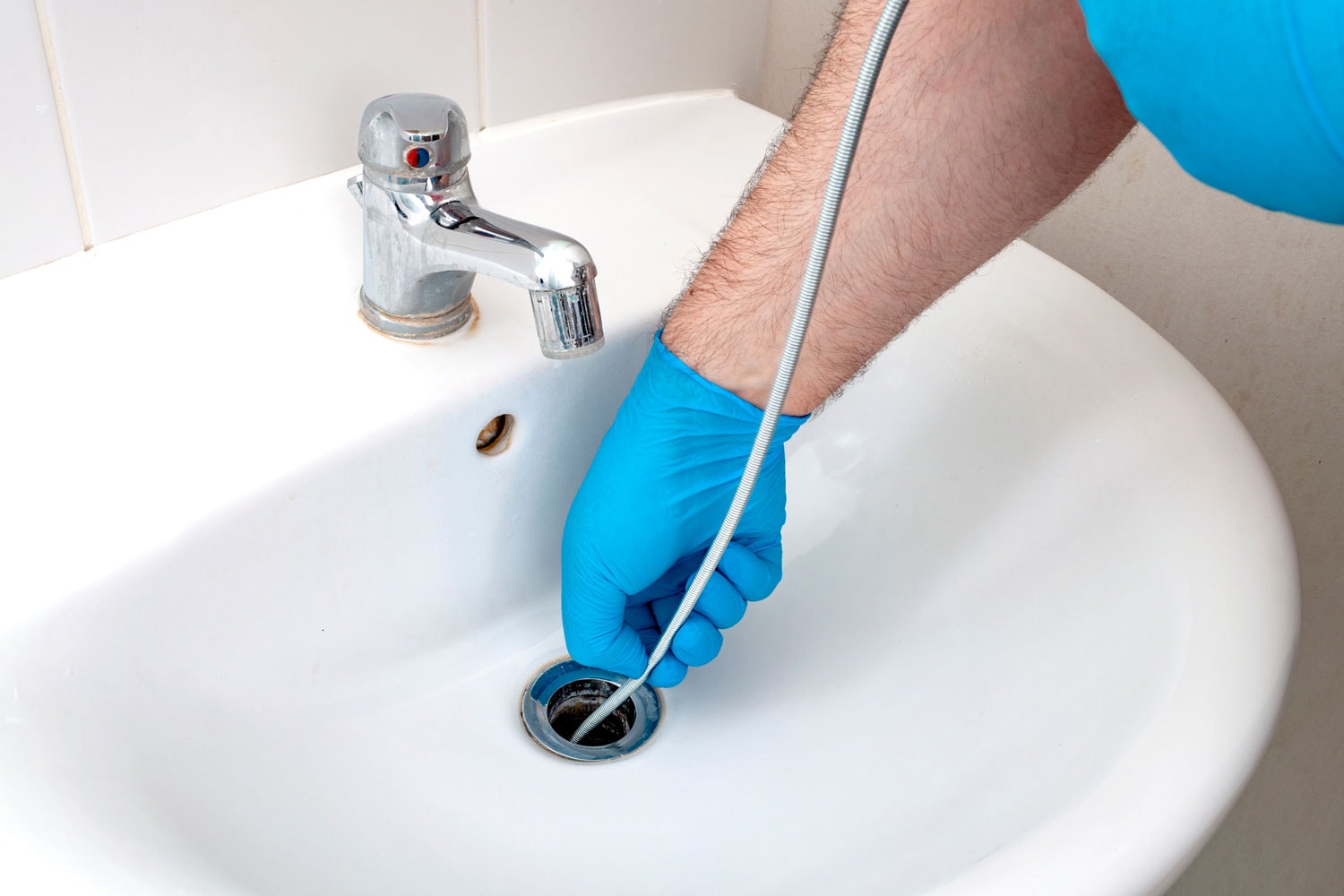 Inserting a plumbing snake to the drain to check for clogging