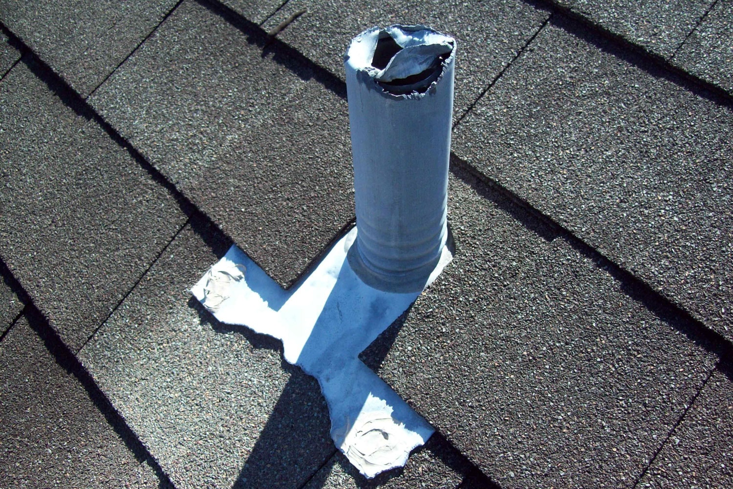 White plumbing colored vent in a roof with asphalt shingle roofing